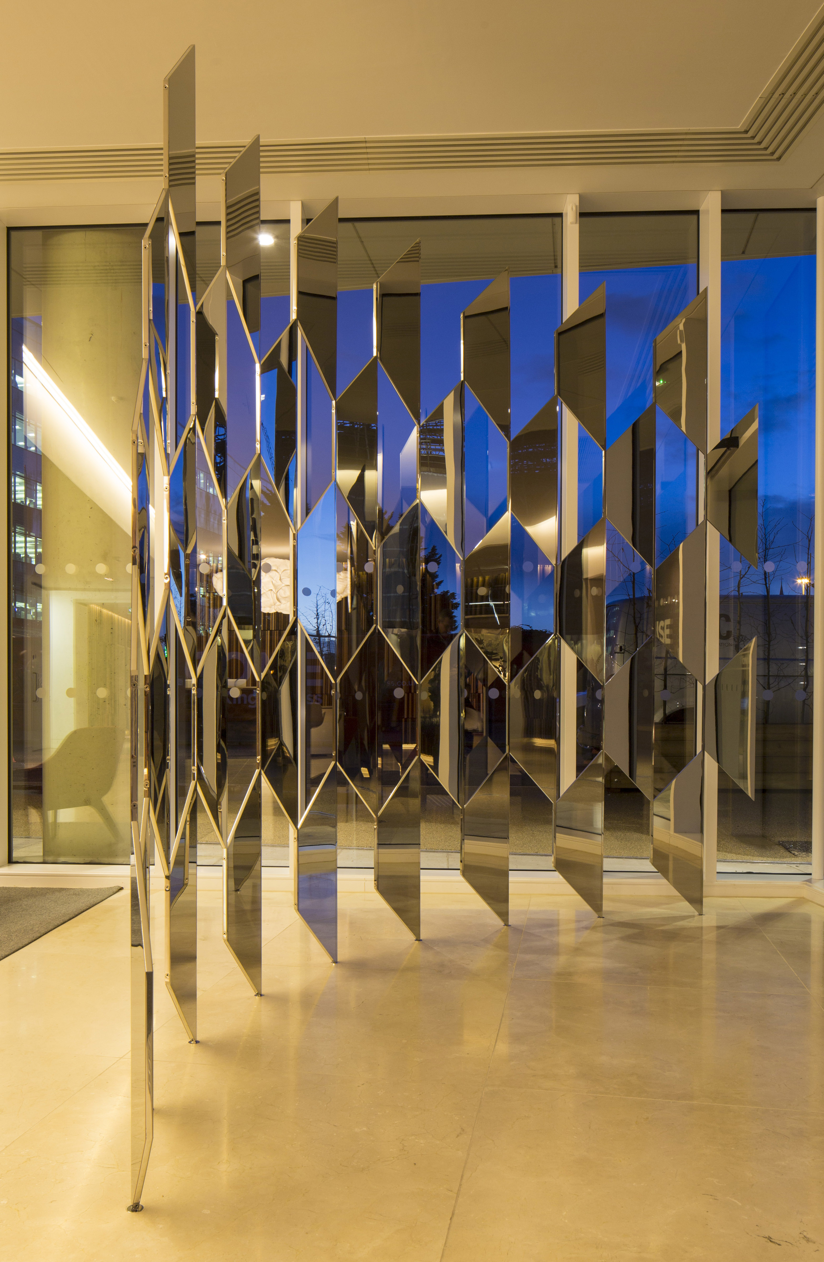 A wide angle shot of an artwork by artist Robert Orchardson. The image depicts two mirror sculptural forms which interlock to create a shifting and repeating hexagonal pattern