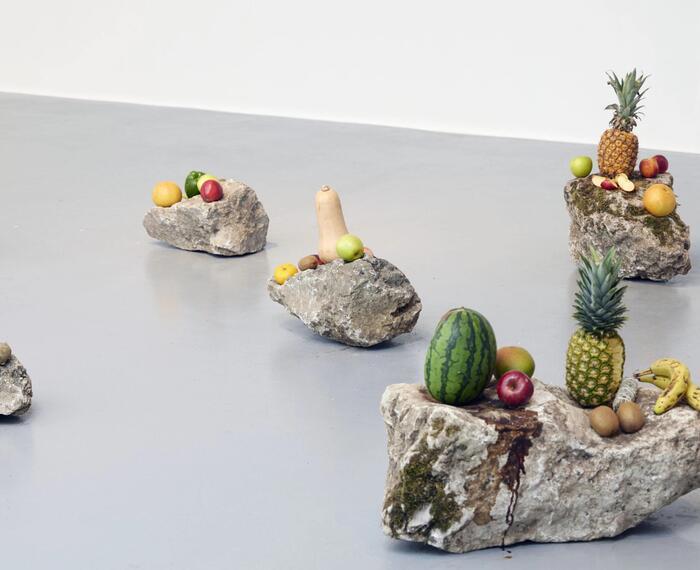 A grey floor with rock sculptures covered in exotic fruits